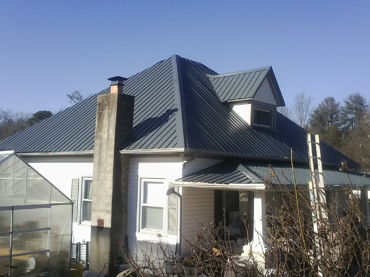 Dark blue standing seam metal roof on a white farmhouse with dormer — Slate & Tile Roof Repair by Roofing Brothers in Kincaid