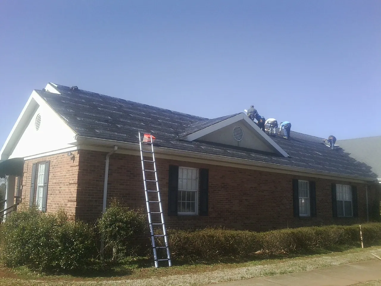 Crew tearing shingles off a brick ranch roof with a ladder set — Metal Roof Repair work by our crew in Kincaid