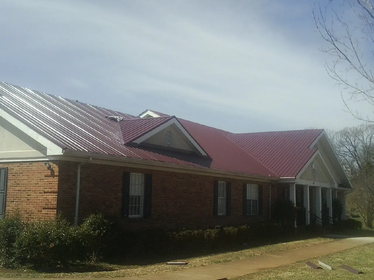 Red metal roof with gabled entries on a long brick building, from a Hail Damage Roof Repair job in Kincaid