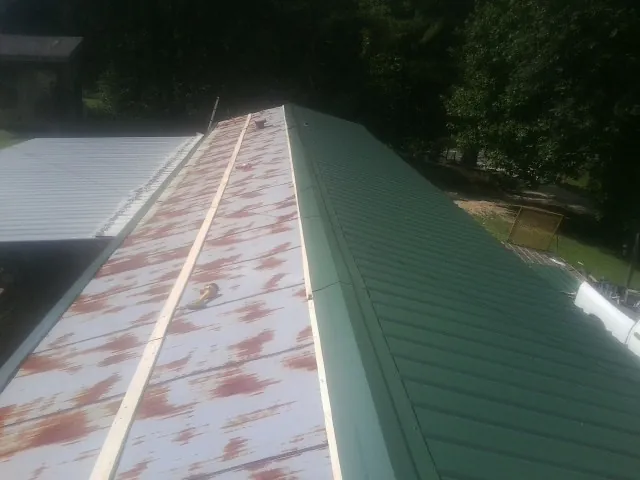 Old rusted panels beside newly installed green metal roofing — Wind Damage Roof Repair by Roofing Brothers in Kincaid