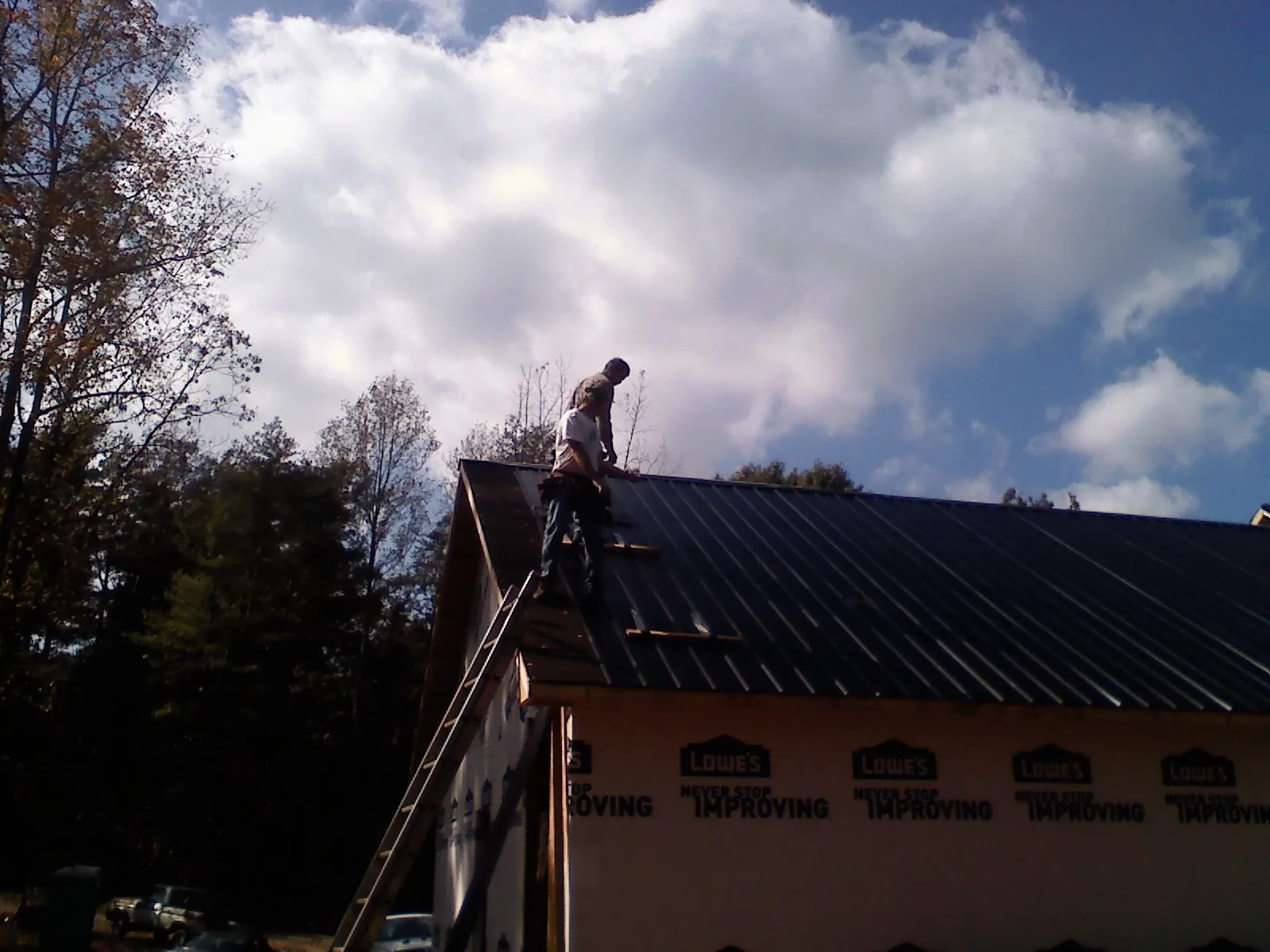 Roofer fastening dark metal panels high against a cloudy sky, from a Roof Inspection job in Kincaid