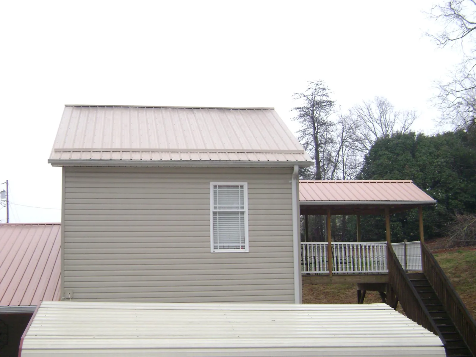 Tan metal roofs on a two story addition and attached porch, from a Roof Replacement job in Kincaid